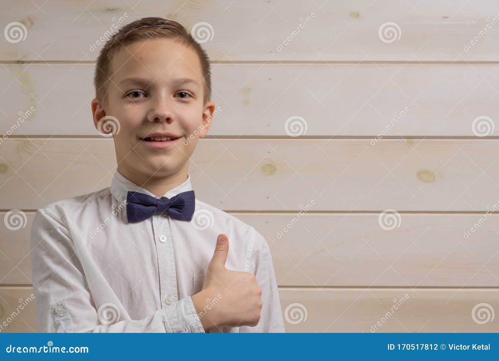 a fair-haired boy of 10 years in a white shirt with the self-tie bow tie smiles against the background of a wooden wall. like