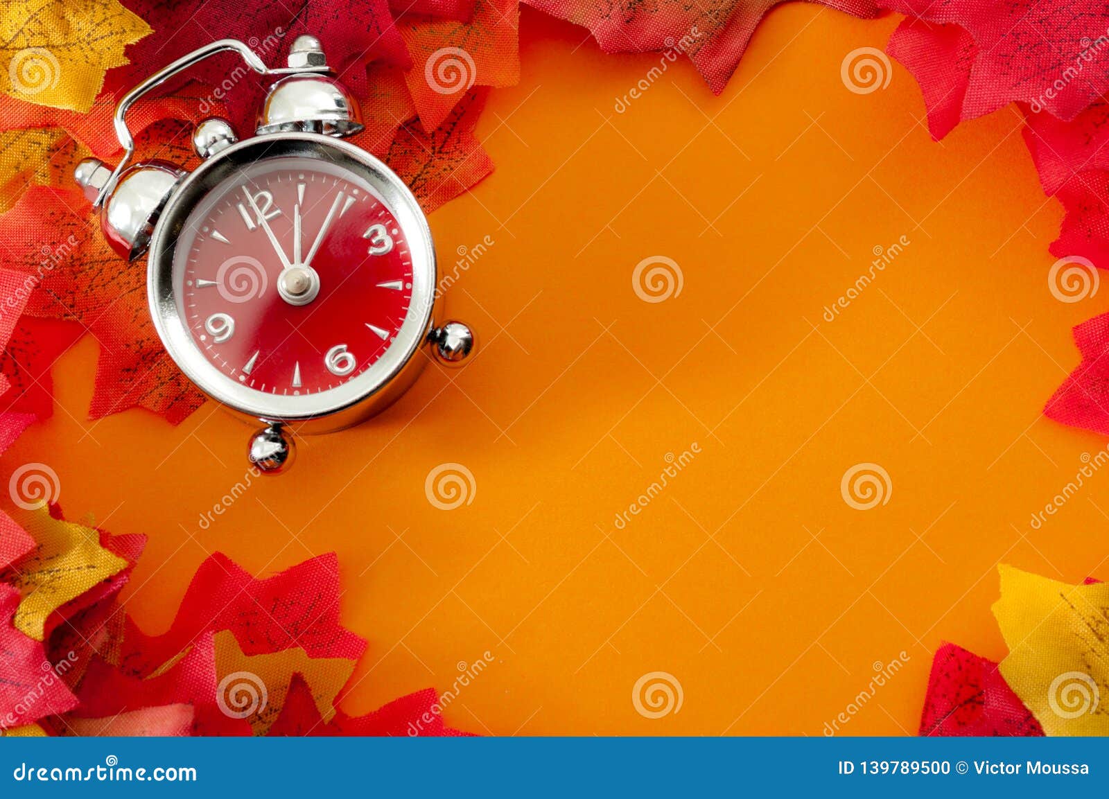 fall back, the end of daylight savings time and turn clocks back on hour concept with a clock surrounded by dried yellow leaves