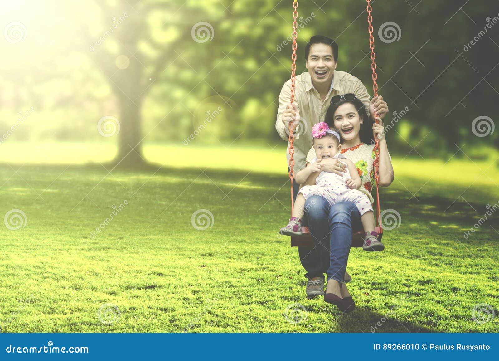 Familia alegre que juega en el oscilación. Retrato de una familia alegre que ríe junto mientras que juega en un oscilación en el parque