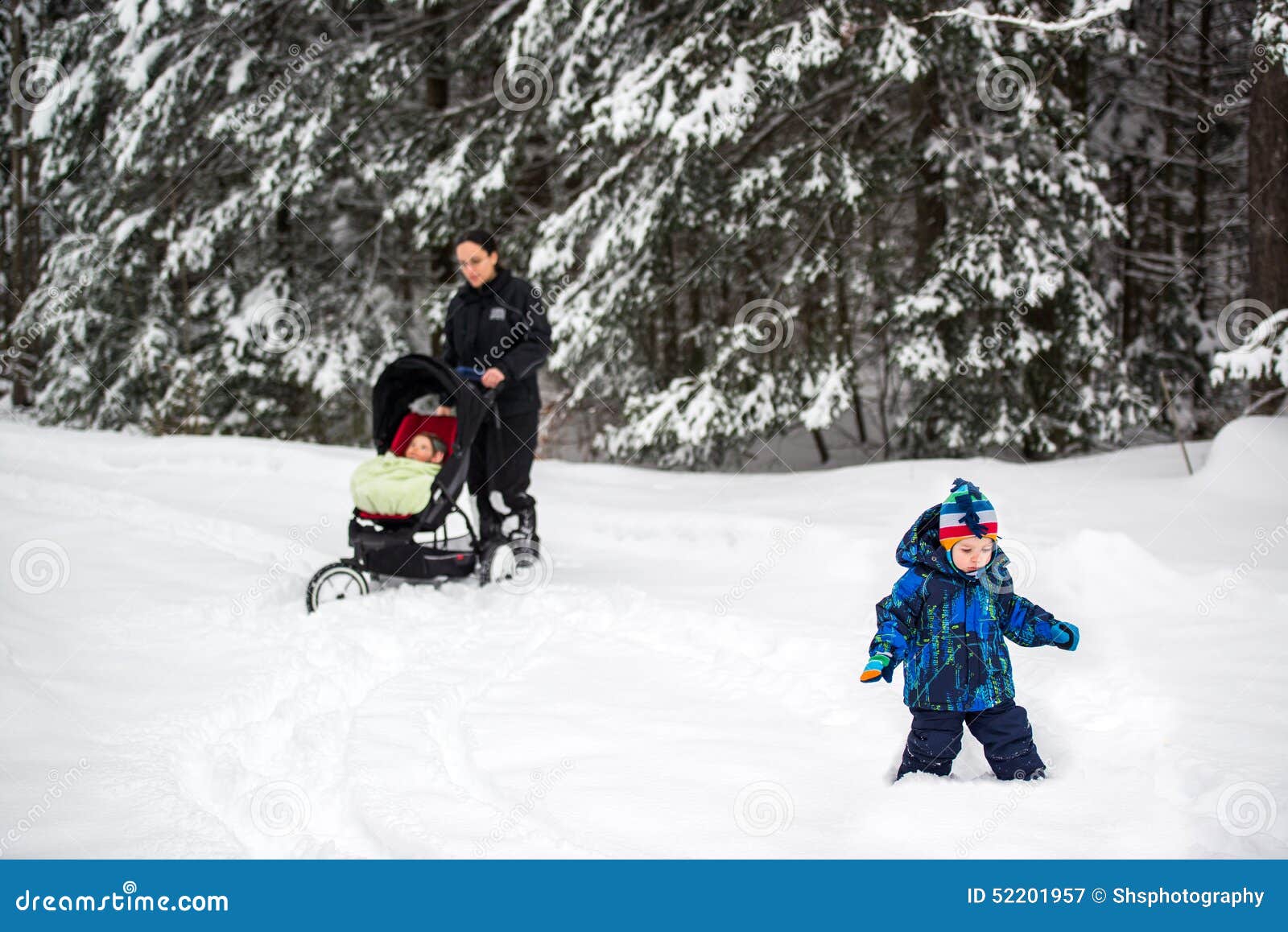 Familia que camina en nieve profunda en un parque. Una madre es en un parque con sus niños después de nevadas grandes Ella empuja a un bebé en un cochecito y su niño intenta caminar en la nieve profunda