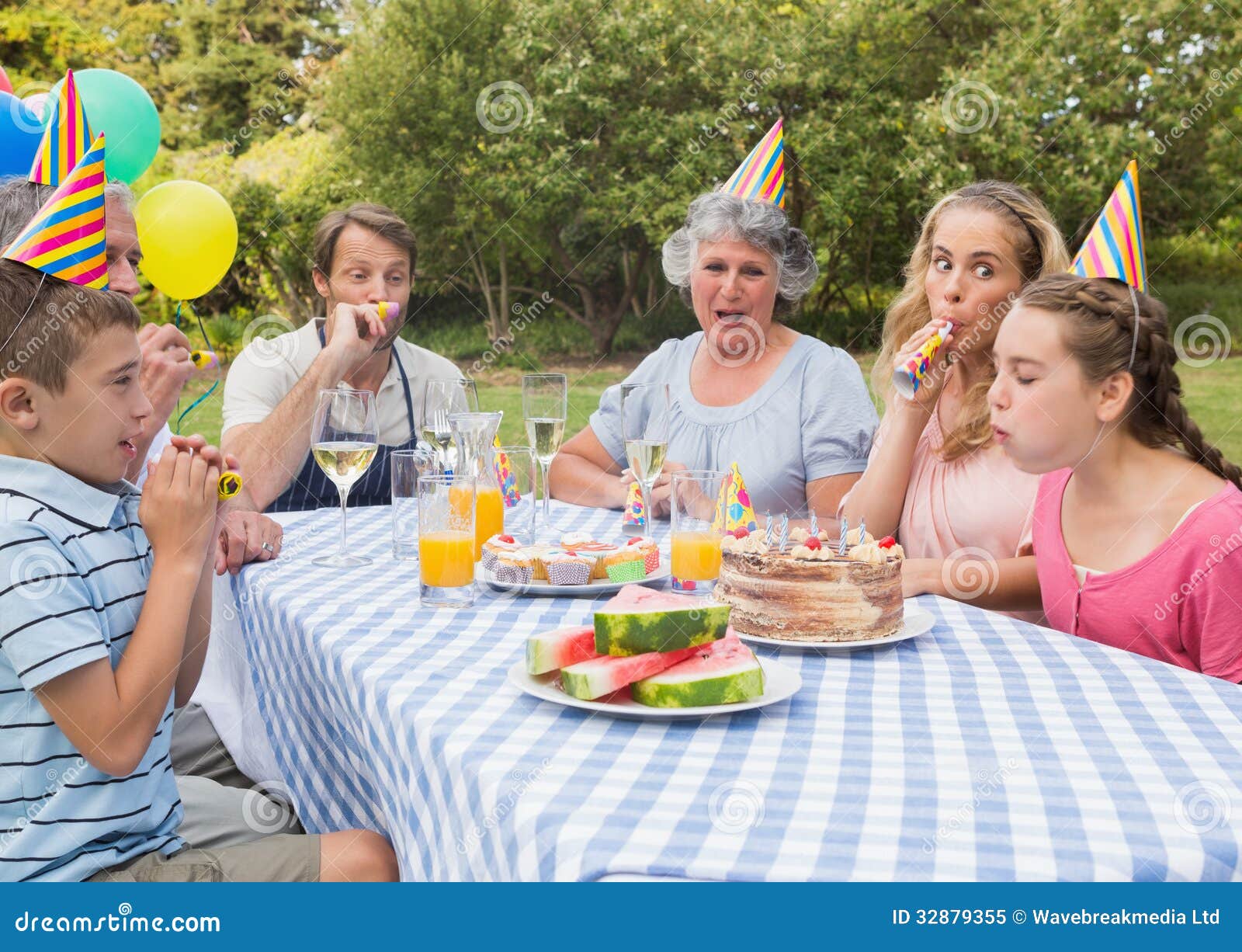 Familie, die draußen Geburtstag der kleinen Mädchen am Picknicktisch feiert. Familie, die draußen Geburtstag der kleinen Mädchen an Schlagparteihörnern des Picknicktischs feiert