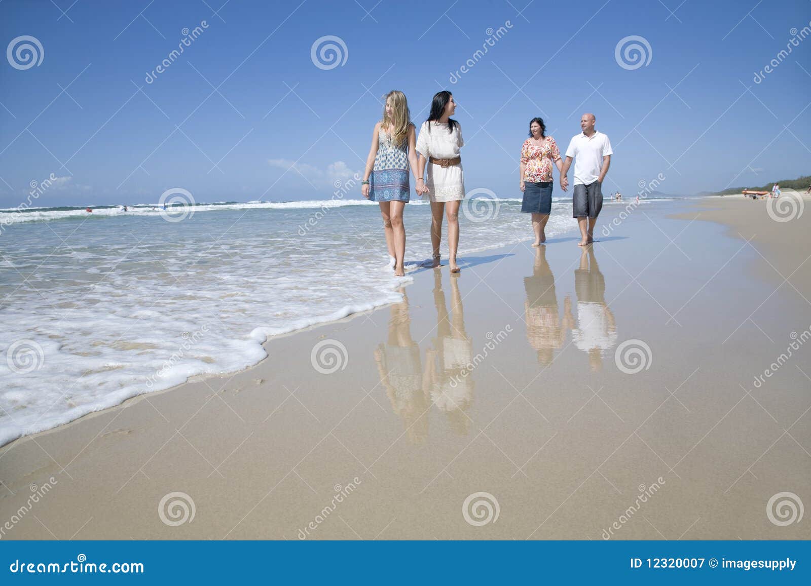 Familj som går på strandholdinghänder på en solig sommardag