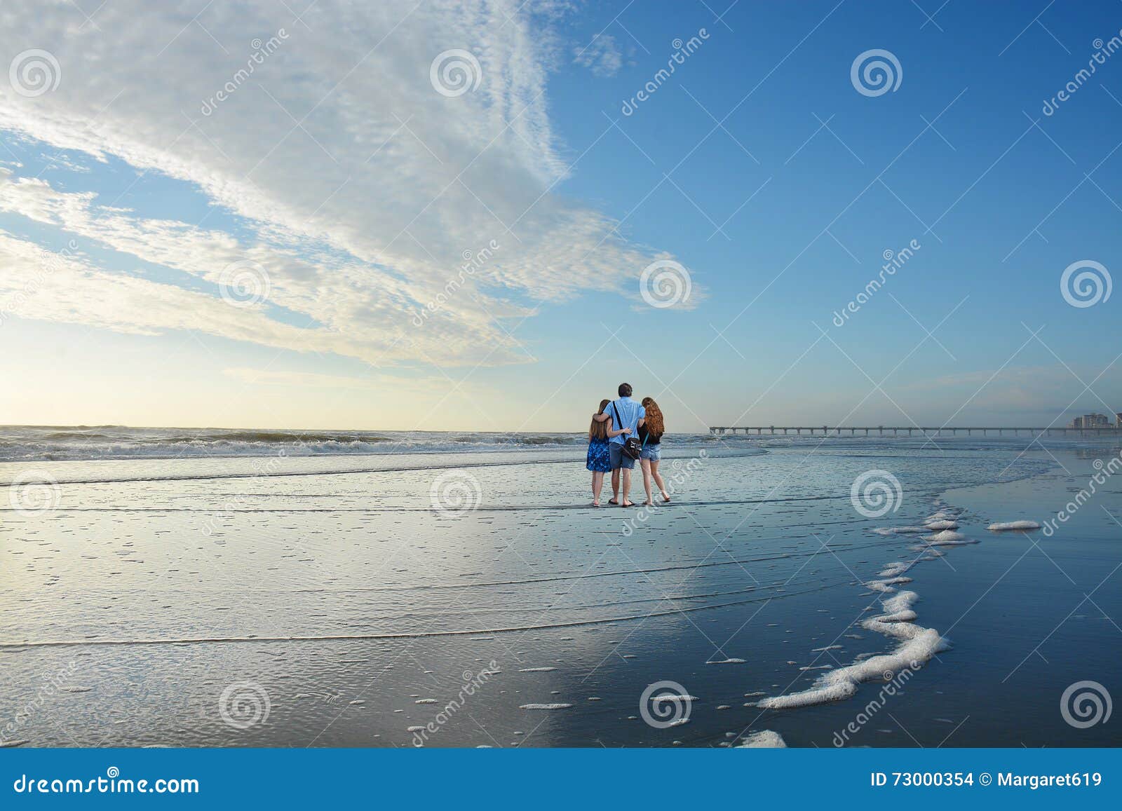 Famille appréciant le temps ensemble sur la belle plage Père avec des bras autour de ses filles Le beau ciel nuageux a réfléchi sur la plage, pilier à l'arrière-plan Copiez l'espace Jacksonville, la Floride, Etats-Unis