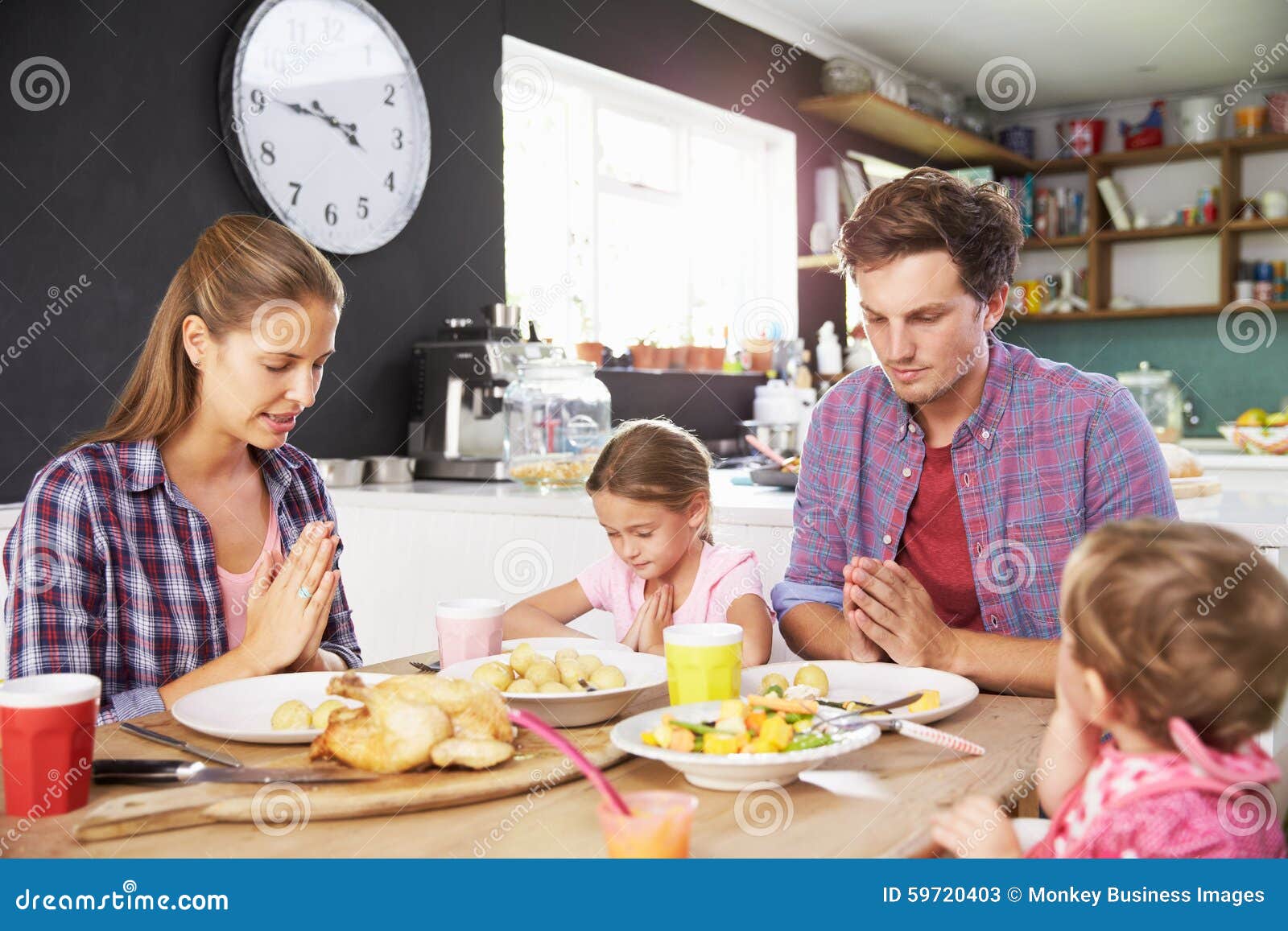 Famille disant la prière avant de manger le repas dans la cuisine ensemble