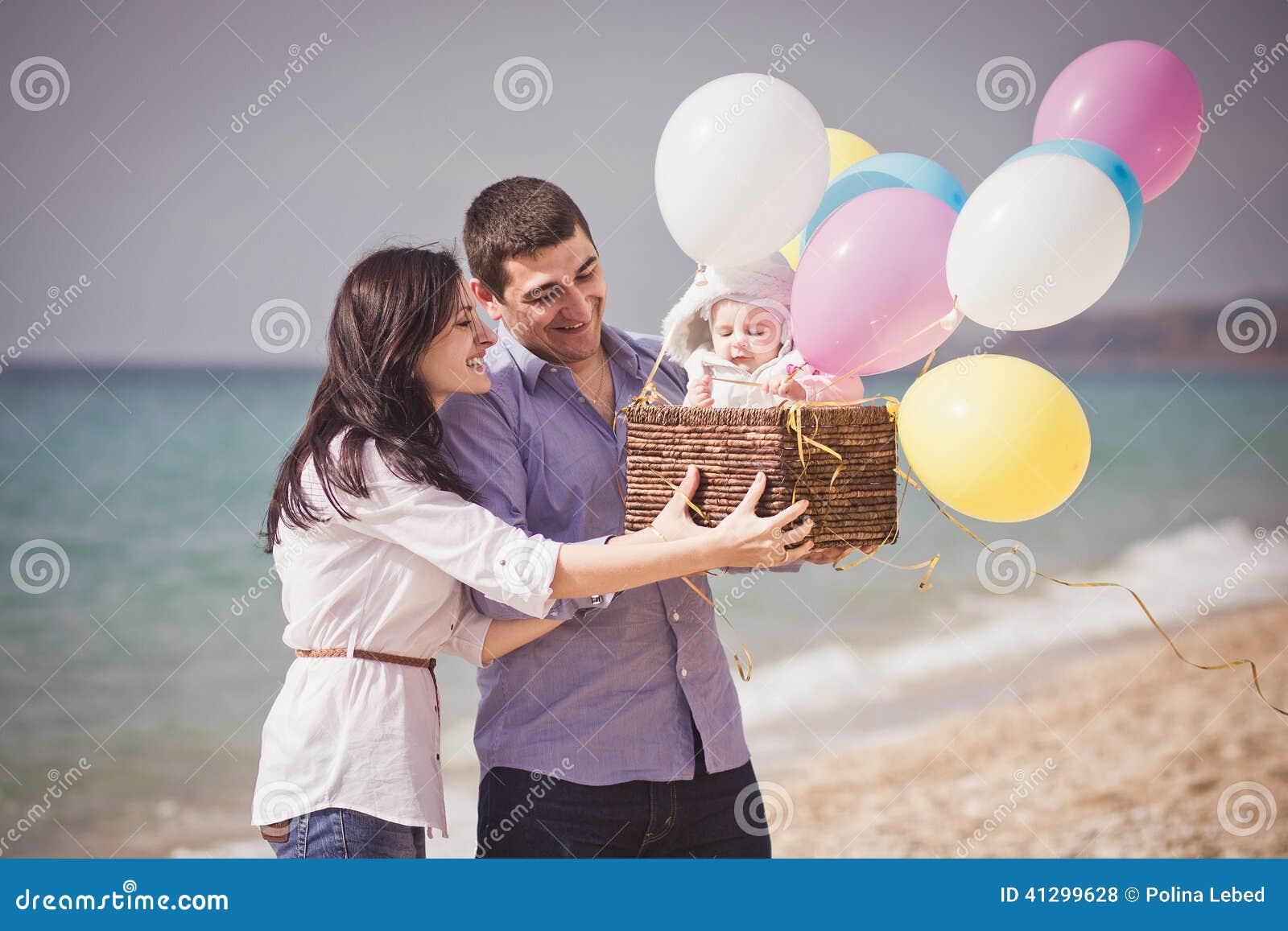 Famille heureuse sur la plage avec les ballons et le panier. Famille heureuse - mère, père et petite fille - sur la plage avec les ballons et le panier