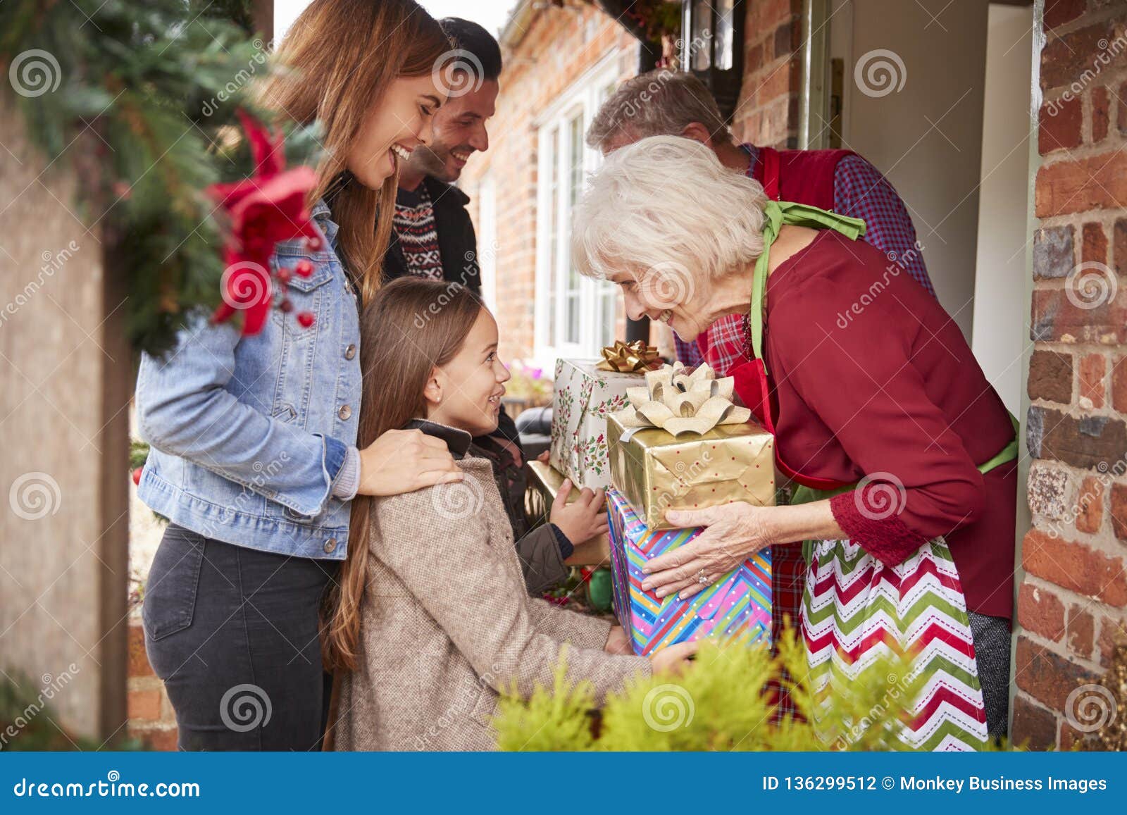 family being greeted by grandparents as they arrive for visit on christmas day with gifts