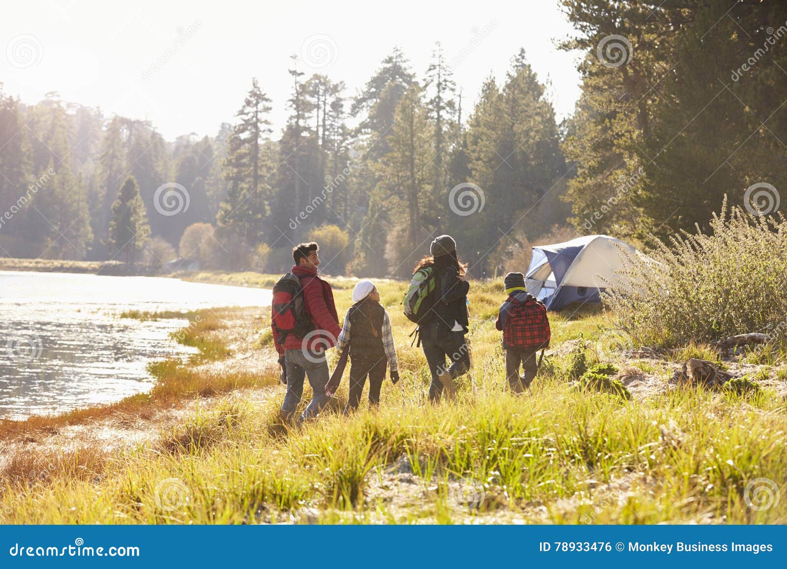 family on a camping trip walking near a lake, back view