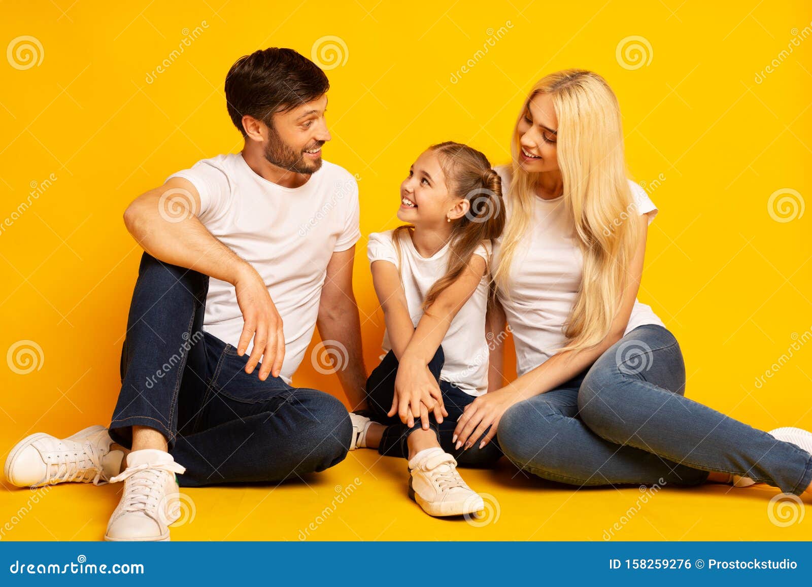 Positive Parents And Daughter Talking Sitting On Floor Over Yellow Background. Family Communication. Parents And Daughter Talking Sitting On Floor Over Yellow Studio Background