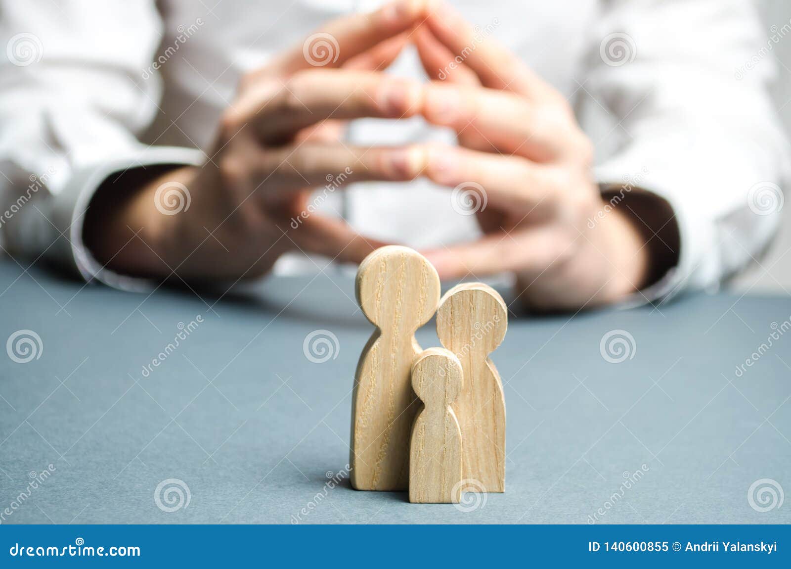 Family Figures And A Man With Hands In The Lock Position In The Background. Typical Family