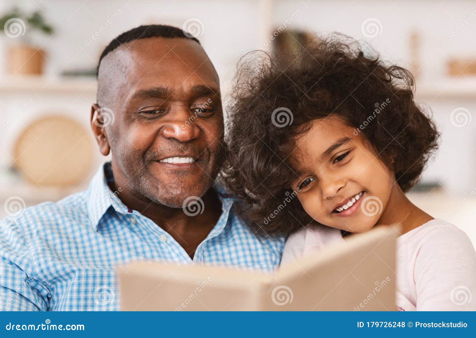 family lockdown hobbies. african american child listening to her grandfather read bedtime story at home