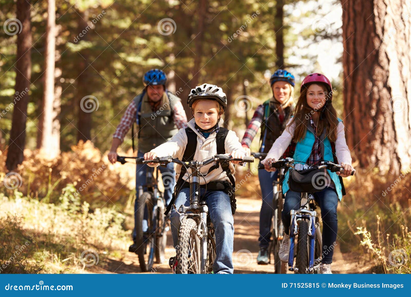 family mountain biking on forest trail, front view