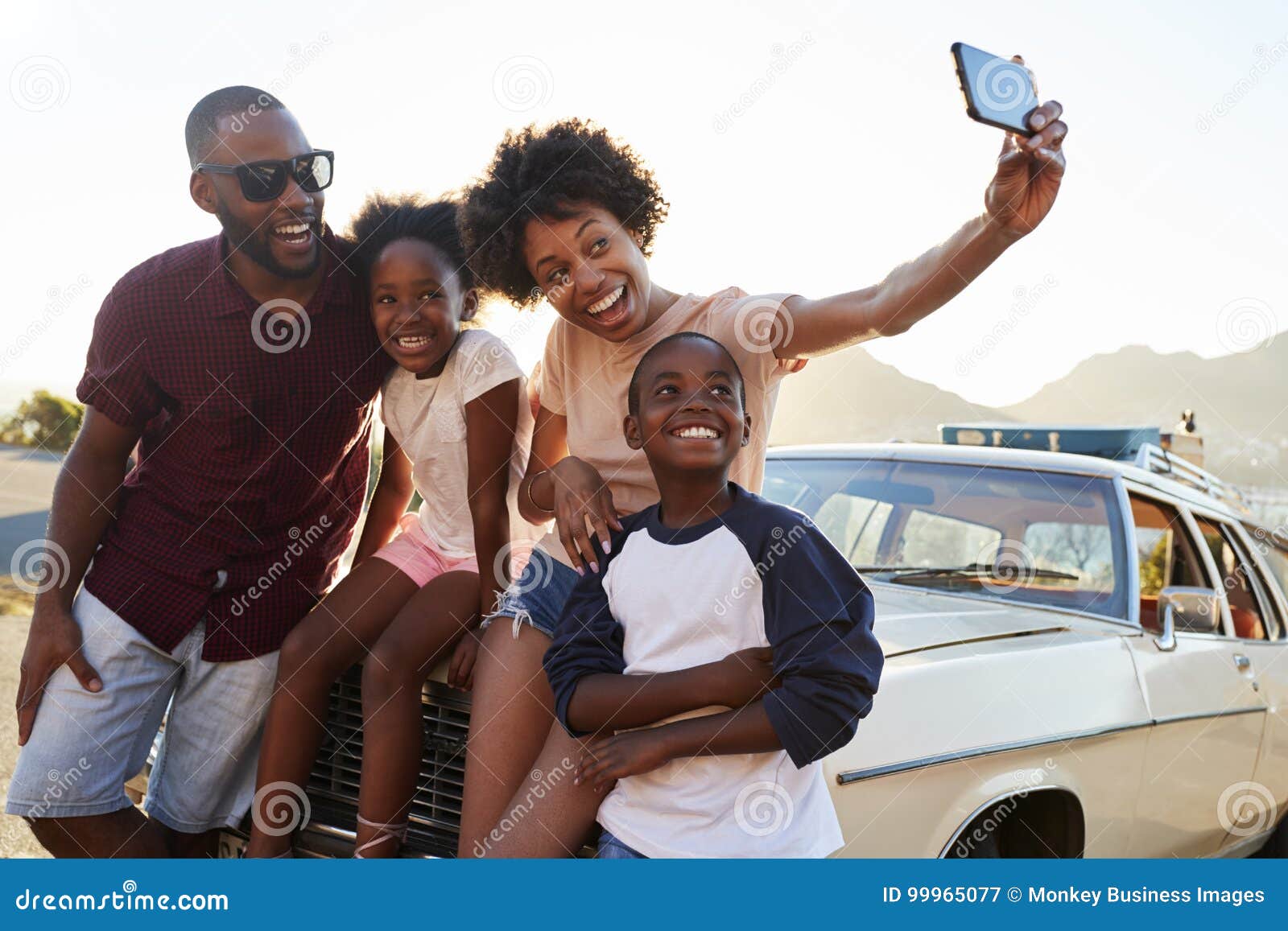 family posing for selfie next to car packed for road trip