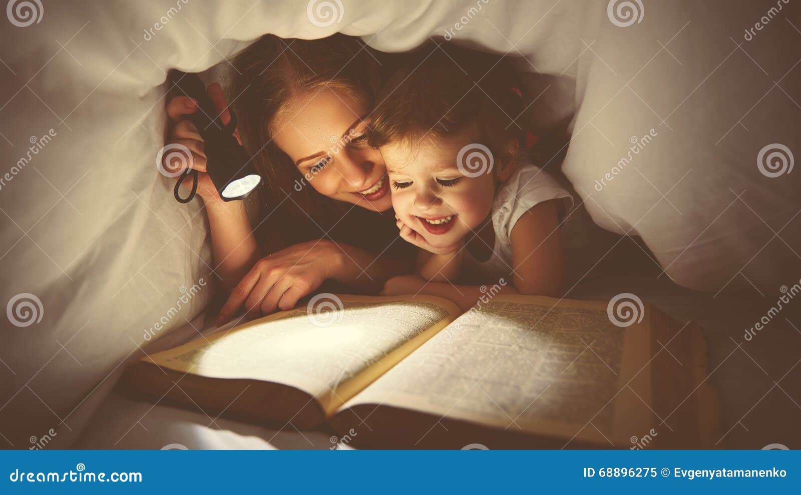 family reading bedtime. mom and child reading book with a flashlight under blanket