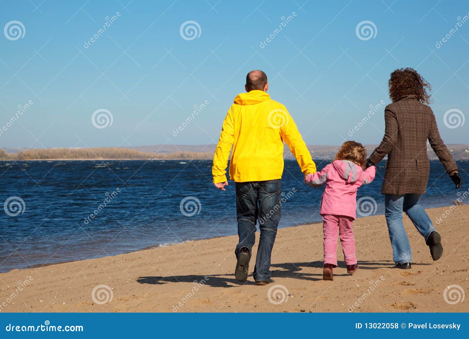 family of three people walking along beach.