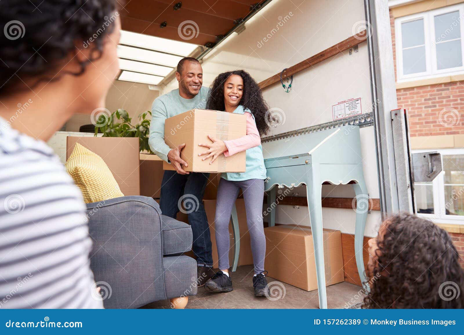 Family Unloading Furniture From Removal Truck Into New Home Stock