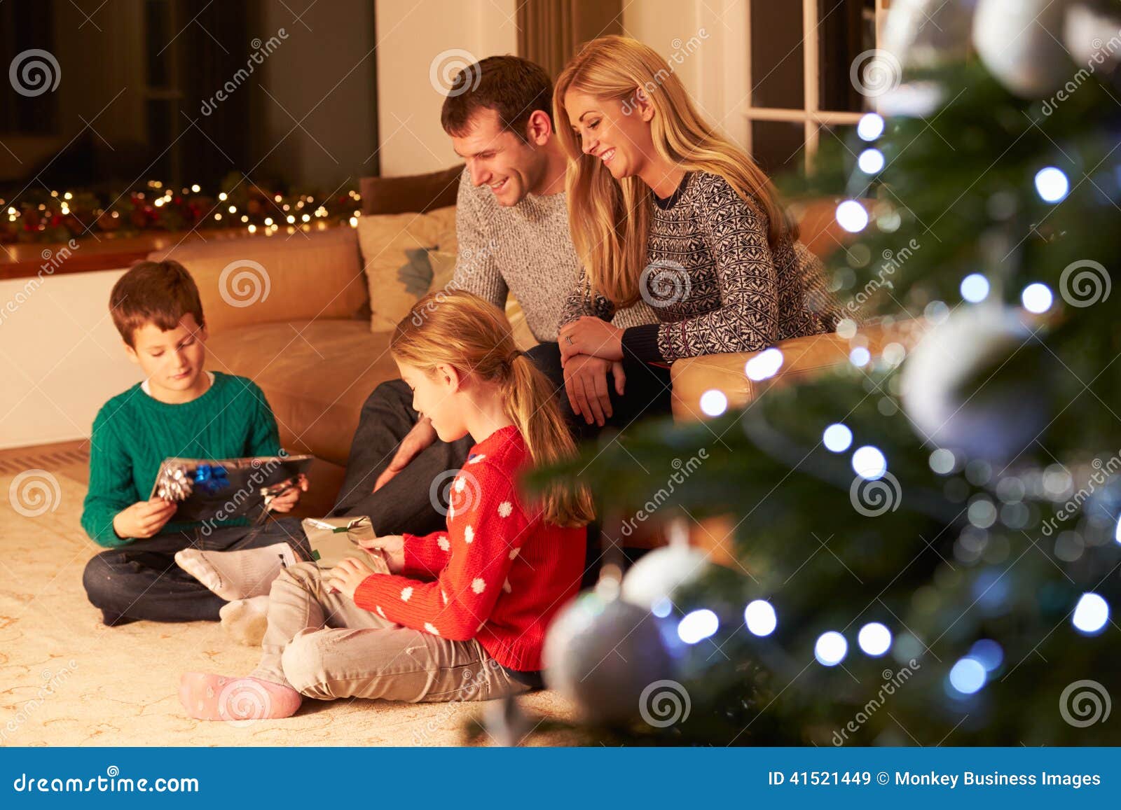 family unwrapping gifts by christmas tree