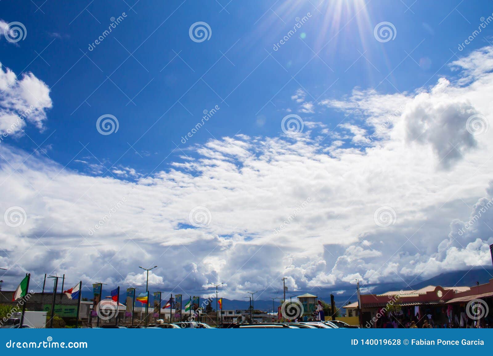 Fantastischer Himmel durch die Wolken über einem touristischen Quadrat. Unter einem großartigen Himmel mit flaumigen Wolken finden Sie einen Marktplatz mit Flaggen