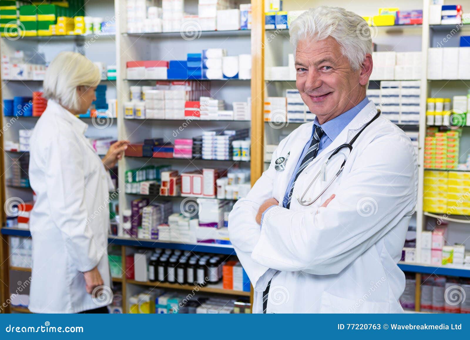 Farmaceuty pozycja z rękami krzyżować i współpracownik sprawdza medycyny w tle przy apteką