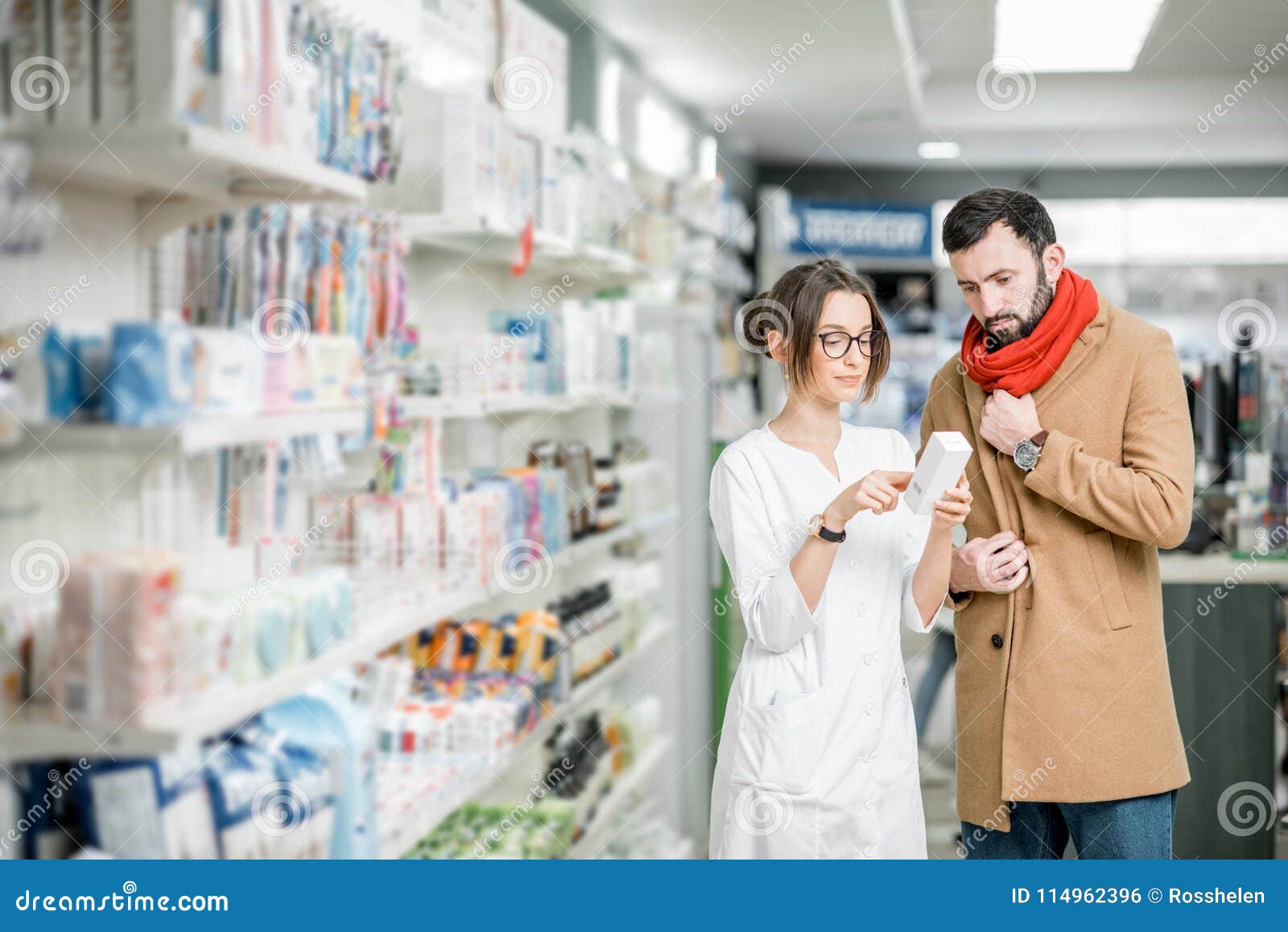 Farmacista con il cliente nel deposito della farmacia. Il farmacista delle giovani donne che sceglie la medicina con il cliente maschio si è vestito in cappotto e sciarpa nel deposito della farmacia