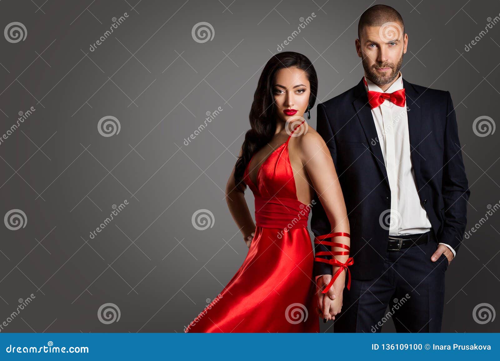 fashion couple, woman and man arms bounded by ribbon, red dress black suit