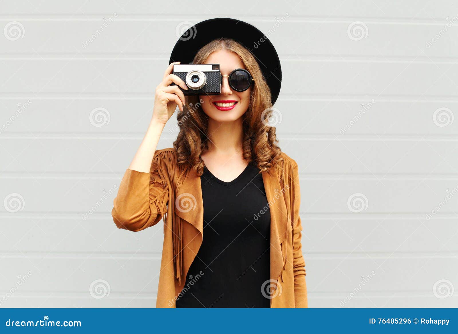 fashion look, pretty cool young woman model with retro film camera wearing a elegant hat, brown jacket, curly hair outdoors
