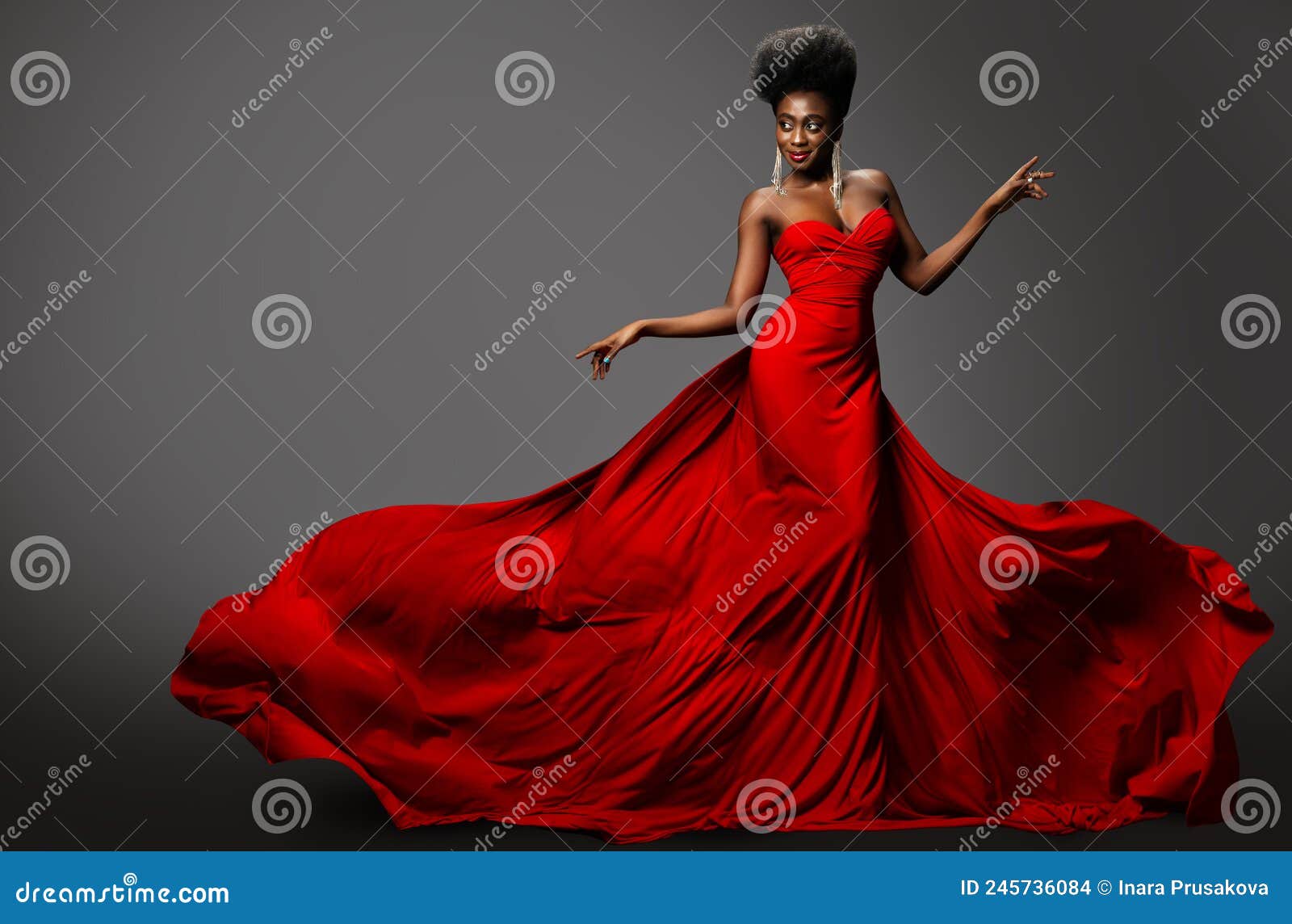 fashion model in red long waving luxury dress. dark skinned beauty woman with afro black hairstyle dancing over gray background.