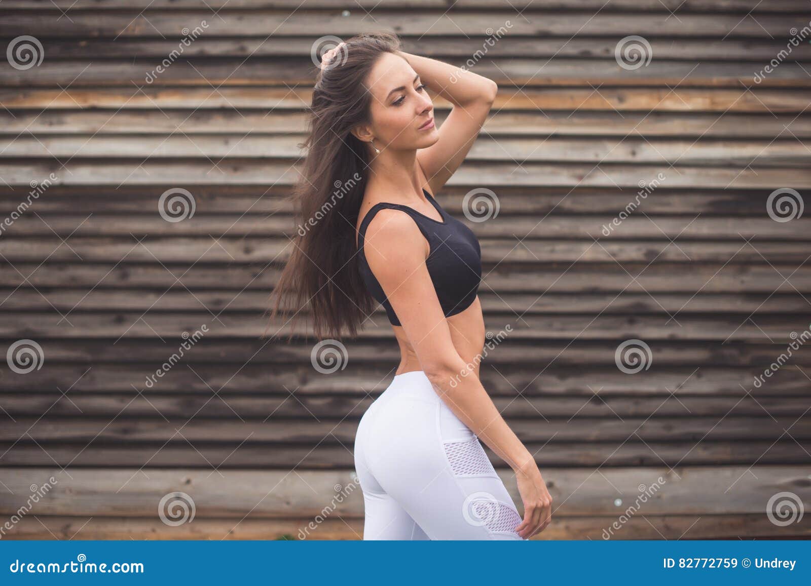 Young athletic woman in sportswear posing in studio against black  background. Ideal female sports figure. Fitness girl with perfect sculpted  muscular and tight body. Stock Photo