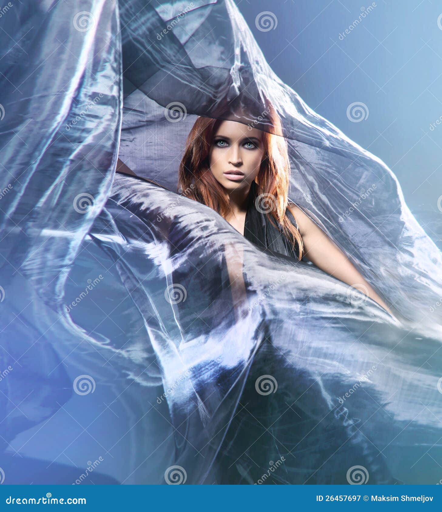 Fashion shoot of a young redhead woman in silk. Fashion shoot of a young and attractive redhead Caucasian woman posing in a blue silk dress. The image is taken on a light blue background.