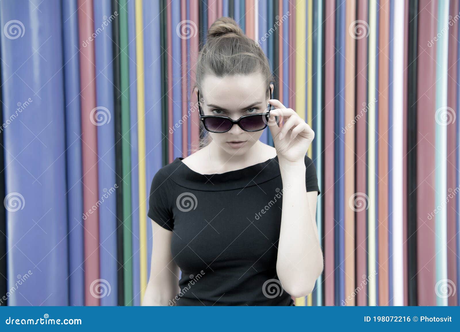 fashion urban style concept. lady mysterious face picking out of black eyeglasses in front of striped colorful wall in