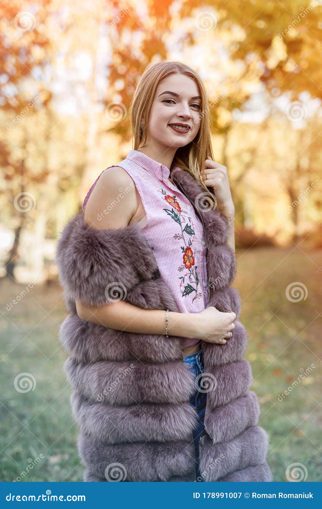 fashion woman. smiling girl in fur coat posin in autumn park with trees and ivy