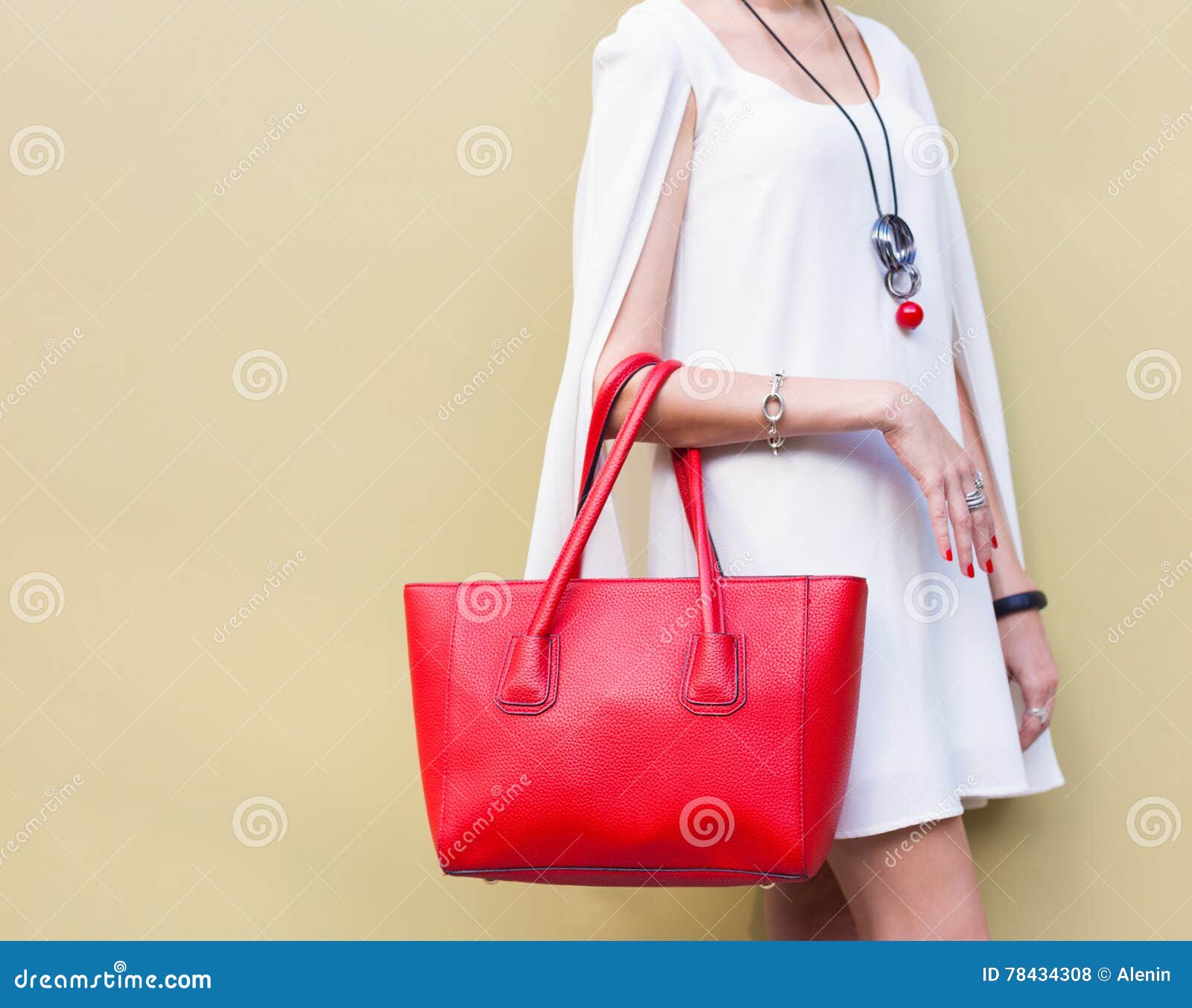 fashionable beautiful big red handbag on the arm of the girl in a fashionable white dress, posing near the wall on a