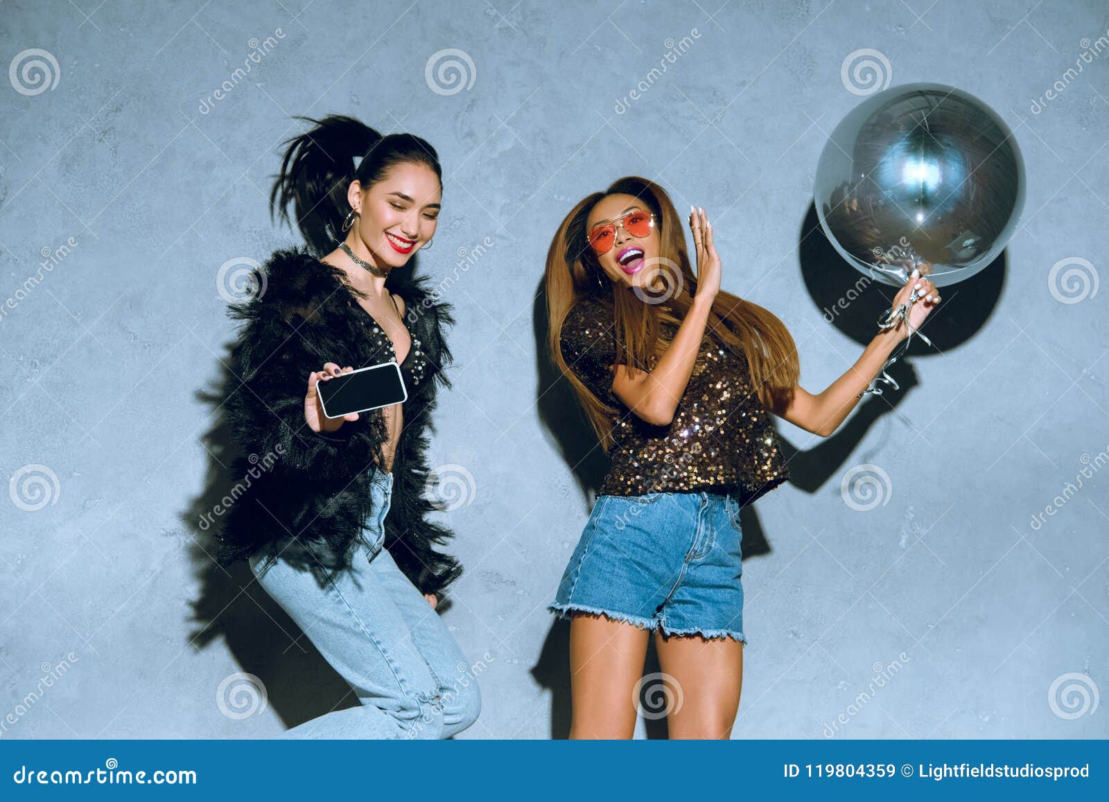 fashionable multiethnic women with smartphone and balloon having fun together