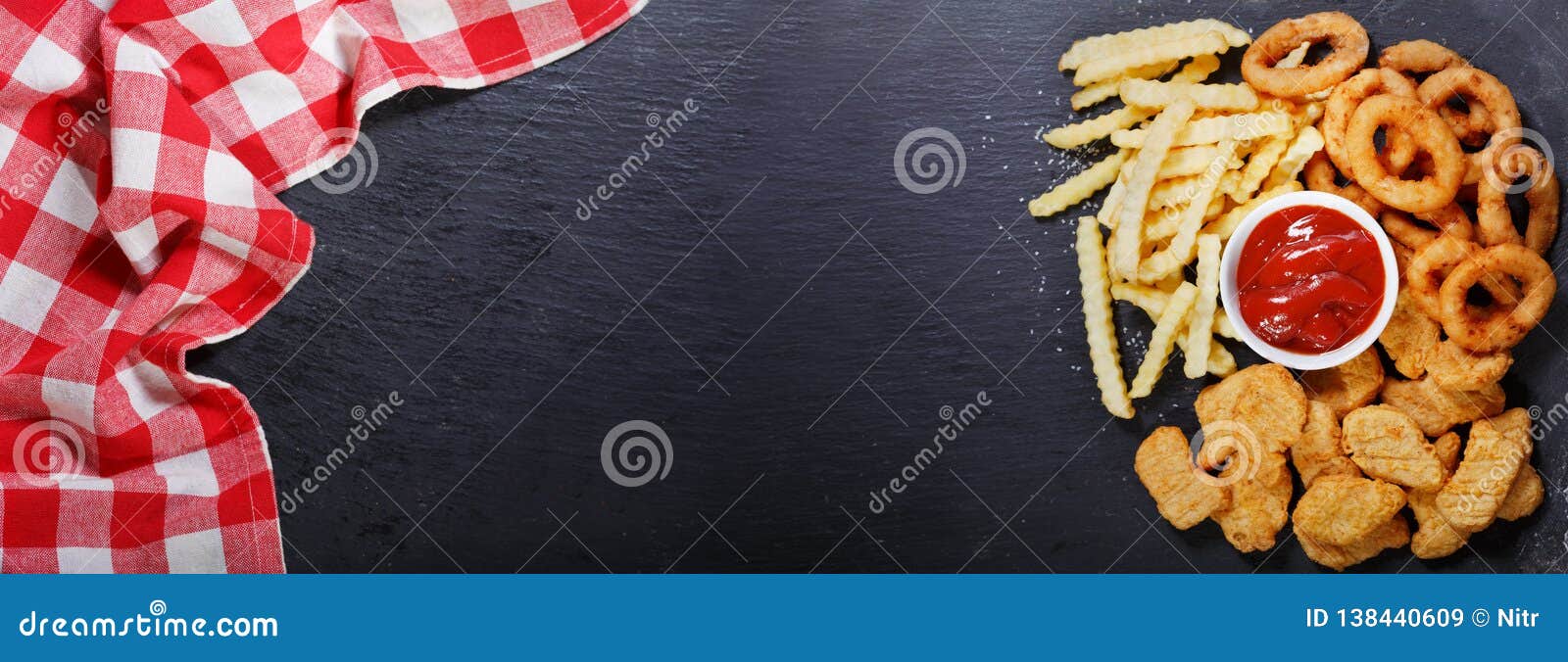 Fast food products: onion rings, french fries and chicken nuggets on dark table, top view