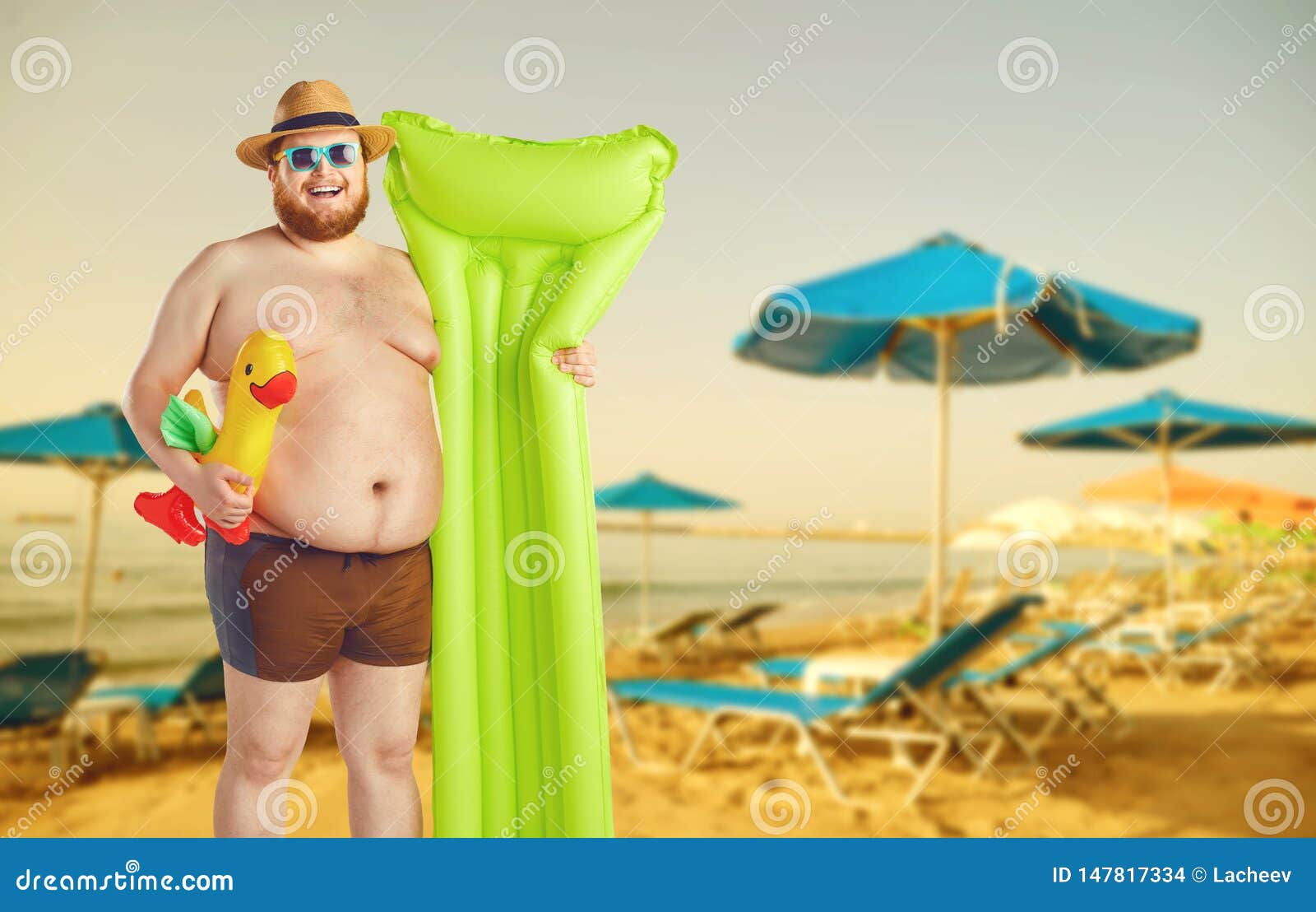 fat funny man in swimming trunks with an inflatable mattress on a gray background.