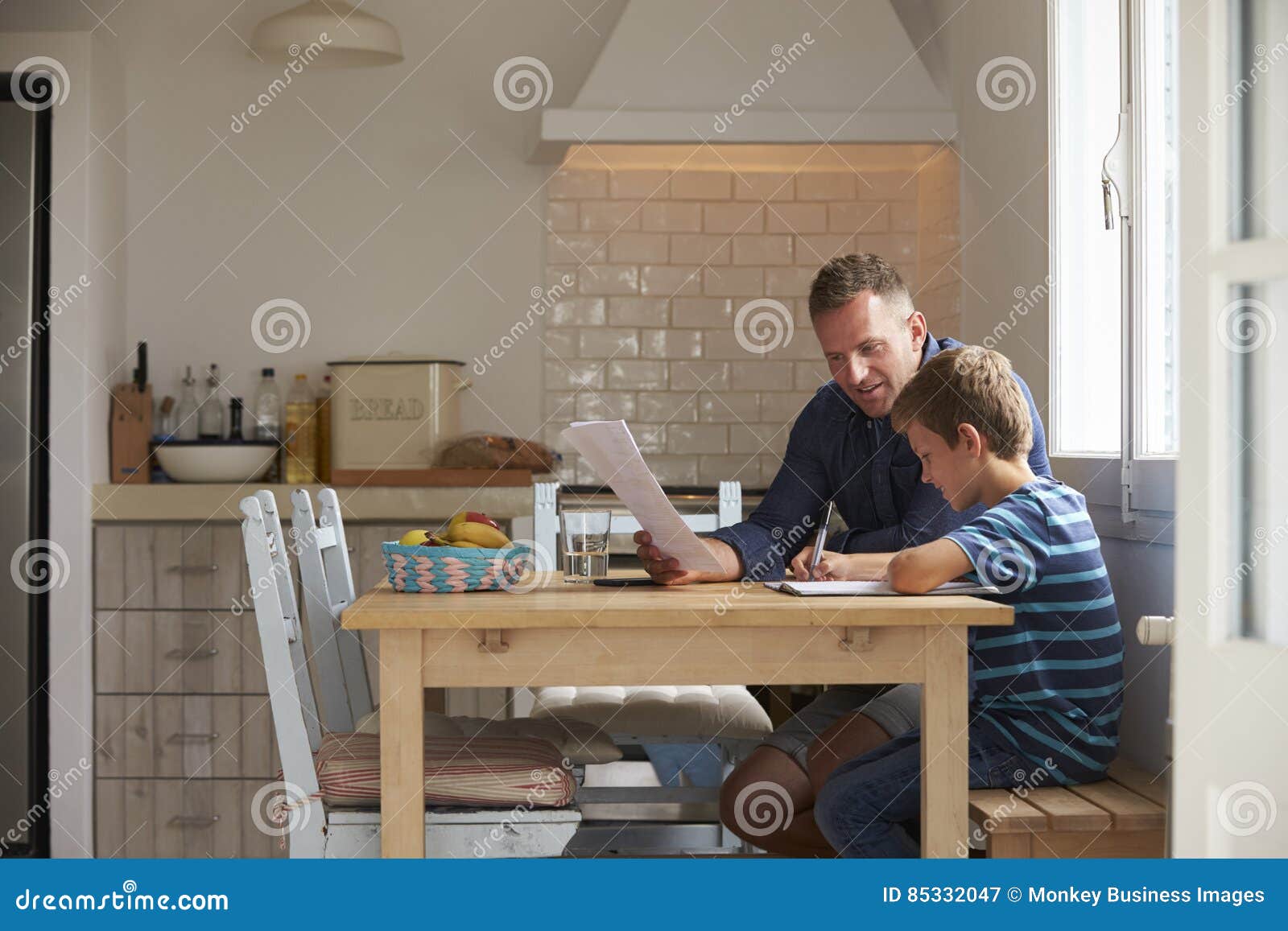 Father Helping Son with Homework Sitting at Kitchen Table Stock Image