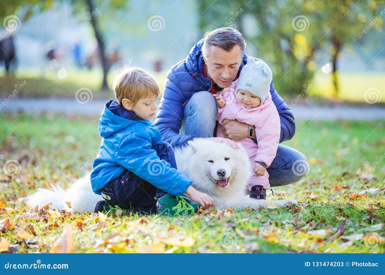 father with preschool son and baby daugther playing with his samoyed dog