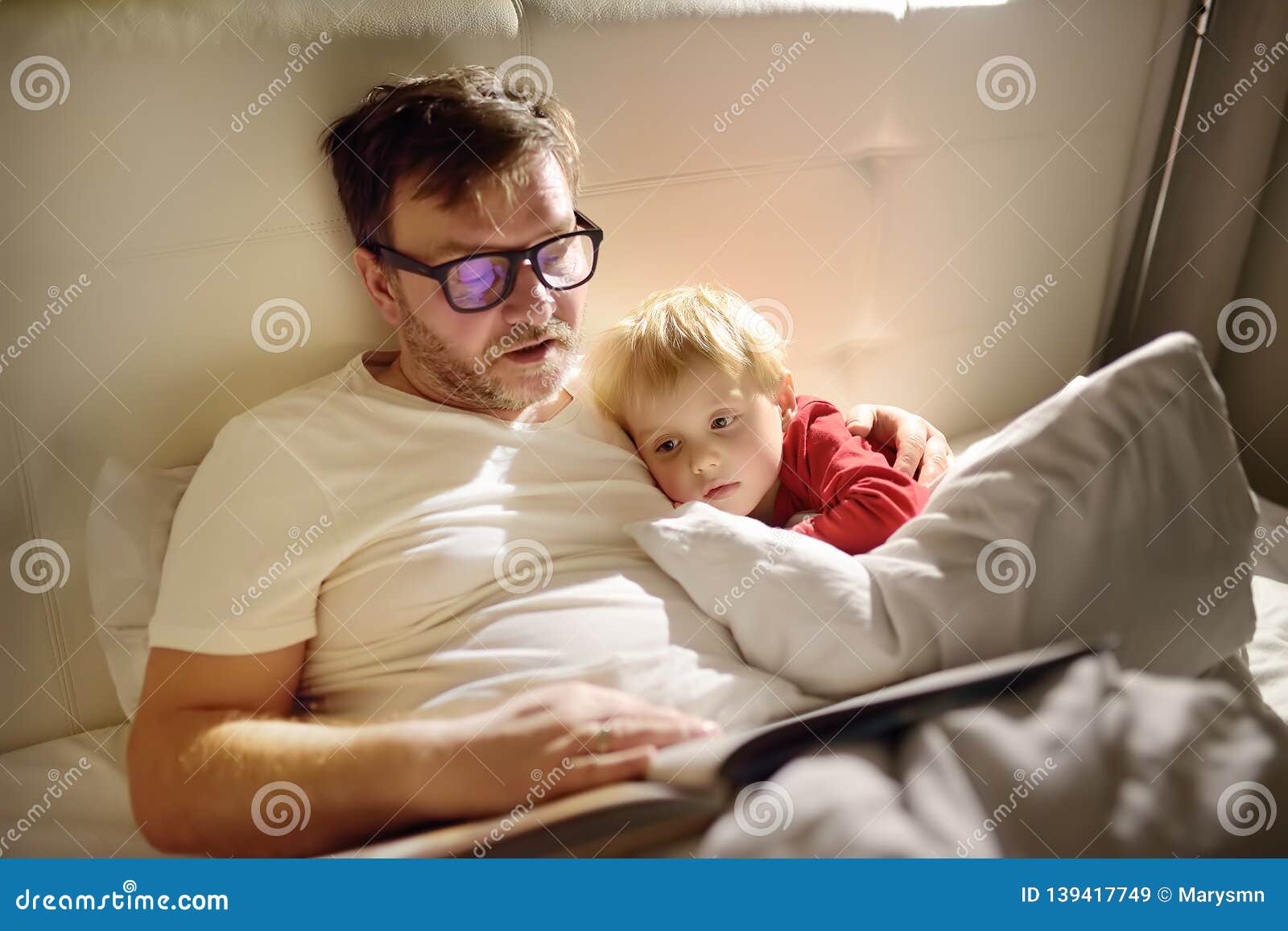 father reading bedtime stories to child. dad putting son to sleep