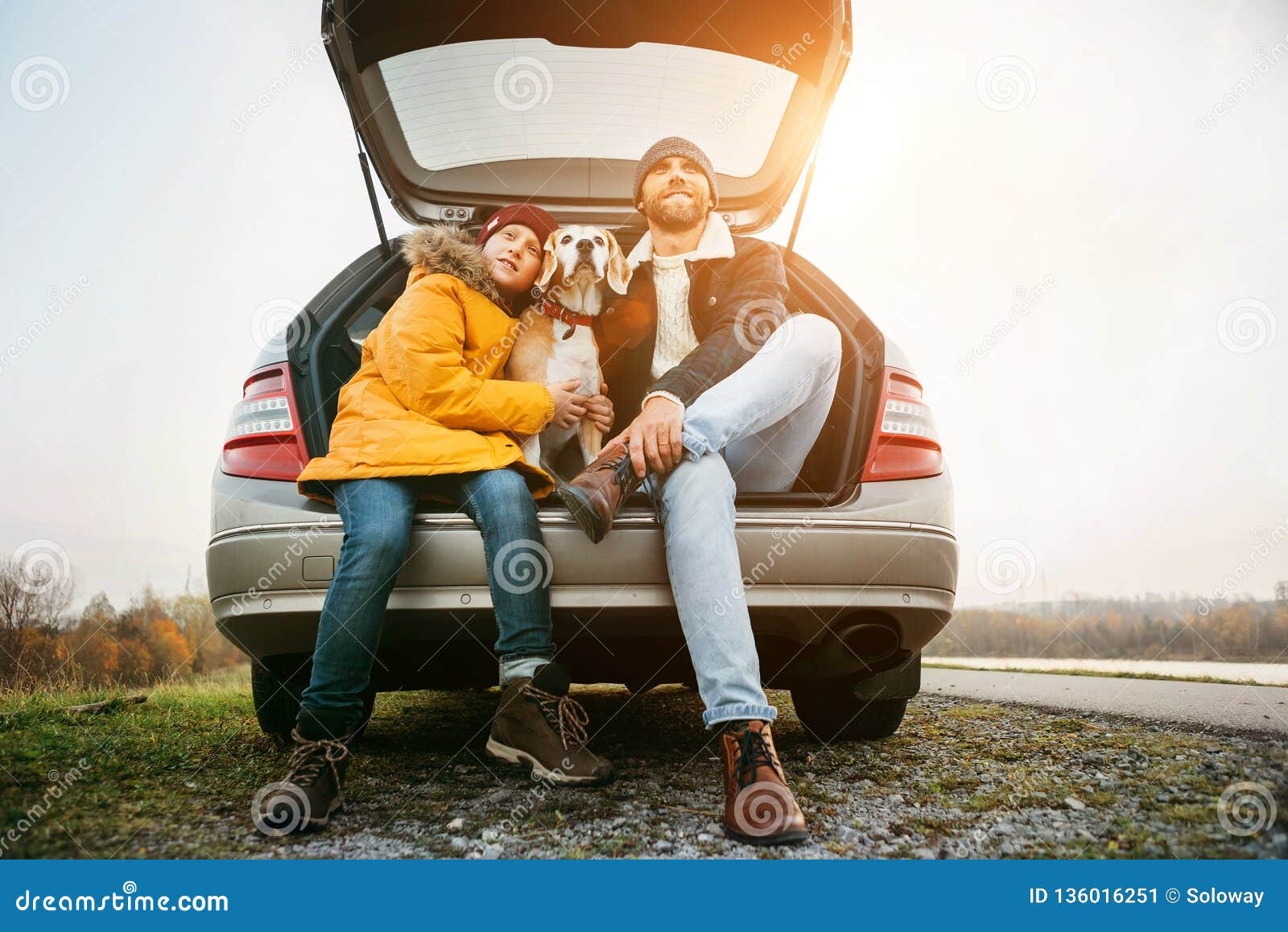 father and son with beagle dog siting together in car trunk. long auto journey break