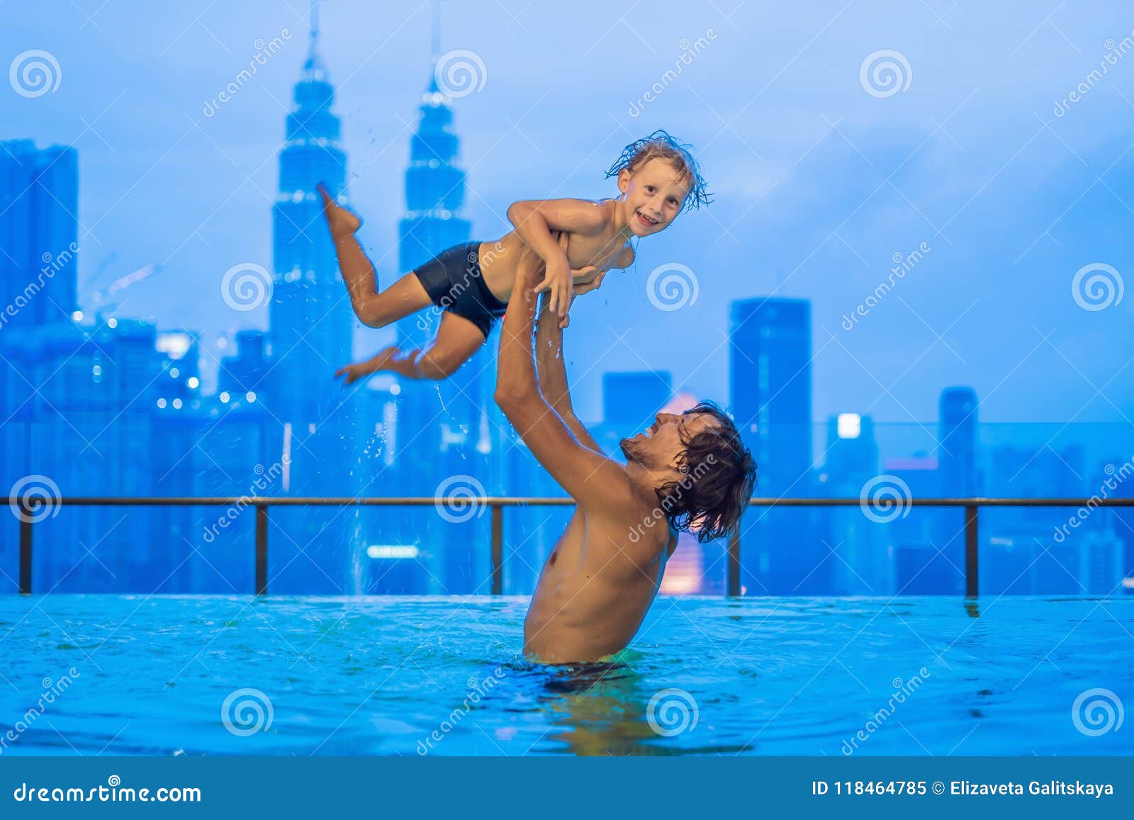 father and son in outdoor swimming pool with city view in blue s