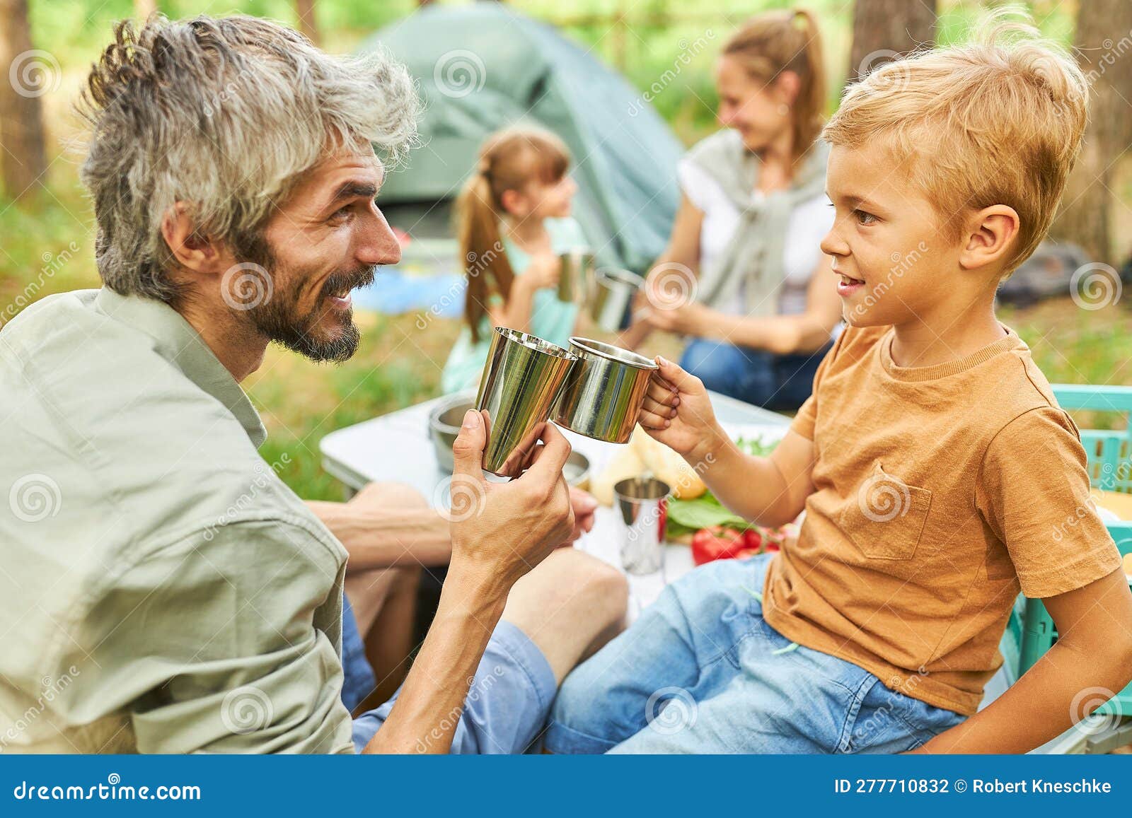 Father and Son Toasting Mugs while Camping in Forest Stock Photo
