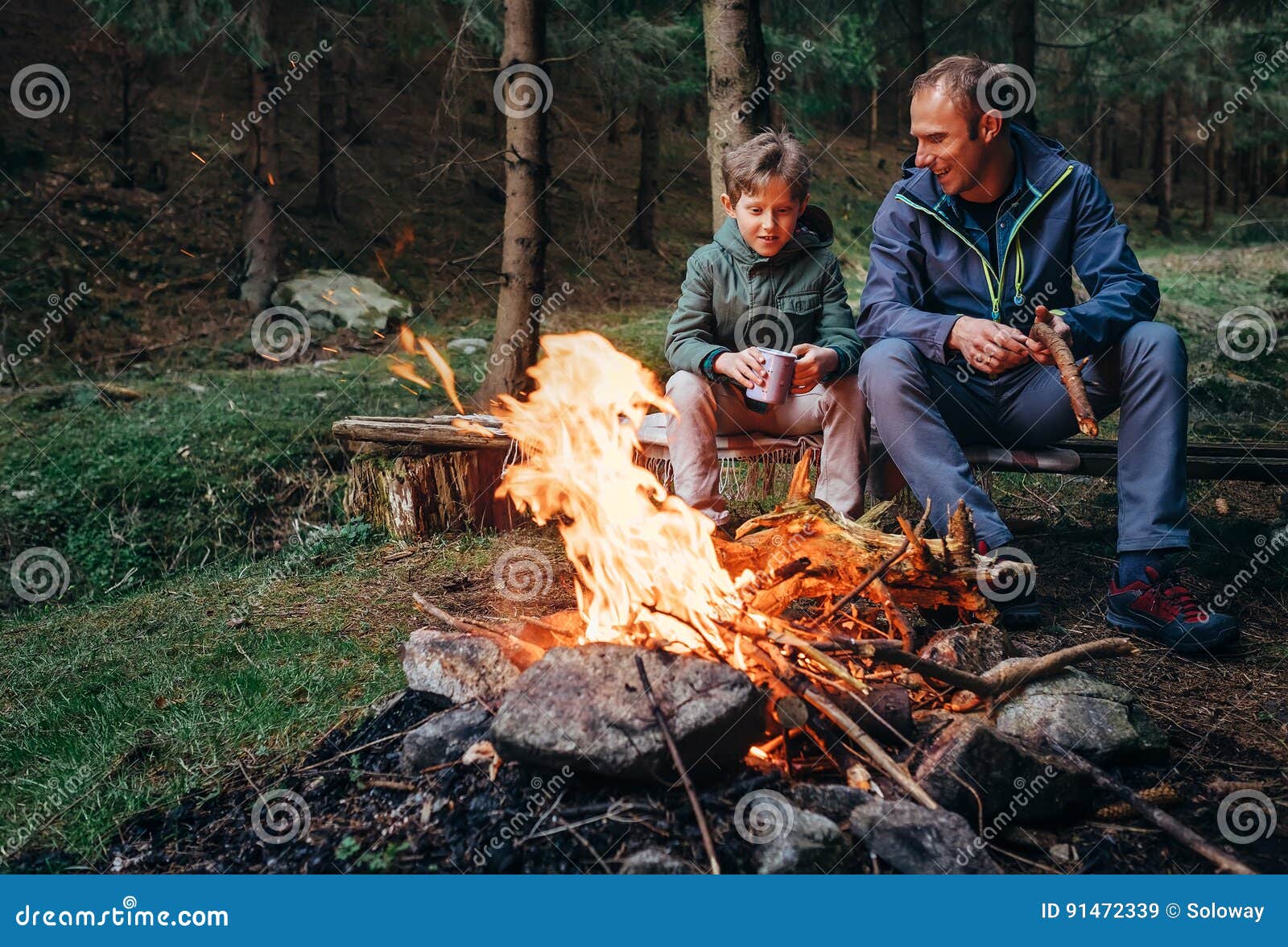 father with son warm near campfire, drink tea and have conversation
