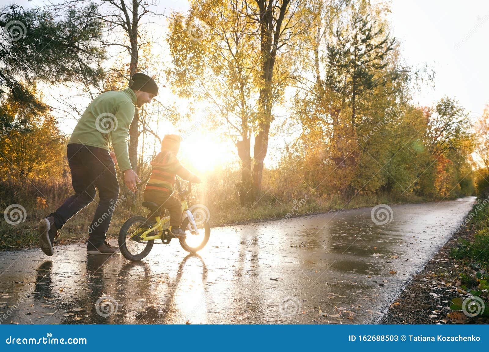 father teaches his little child to ride bike in autumn park. happy family moments. time together dad and son. candid lifestyle