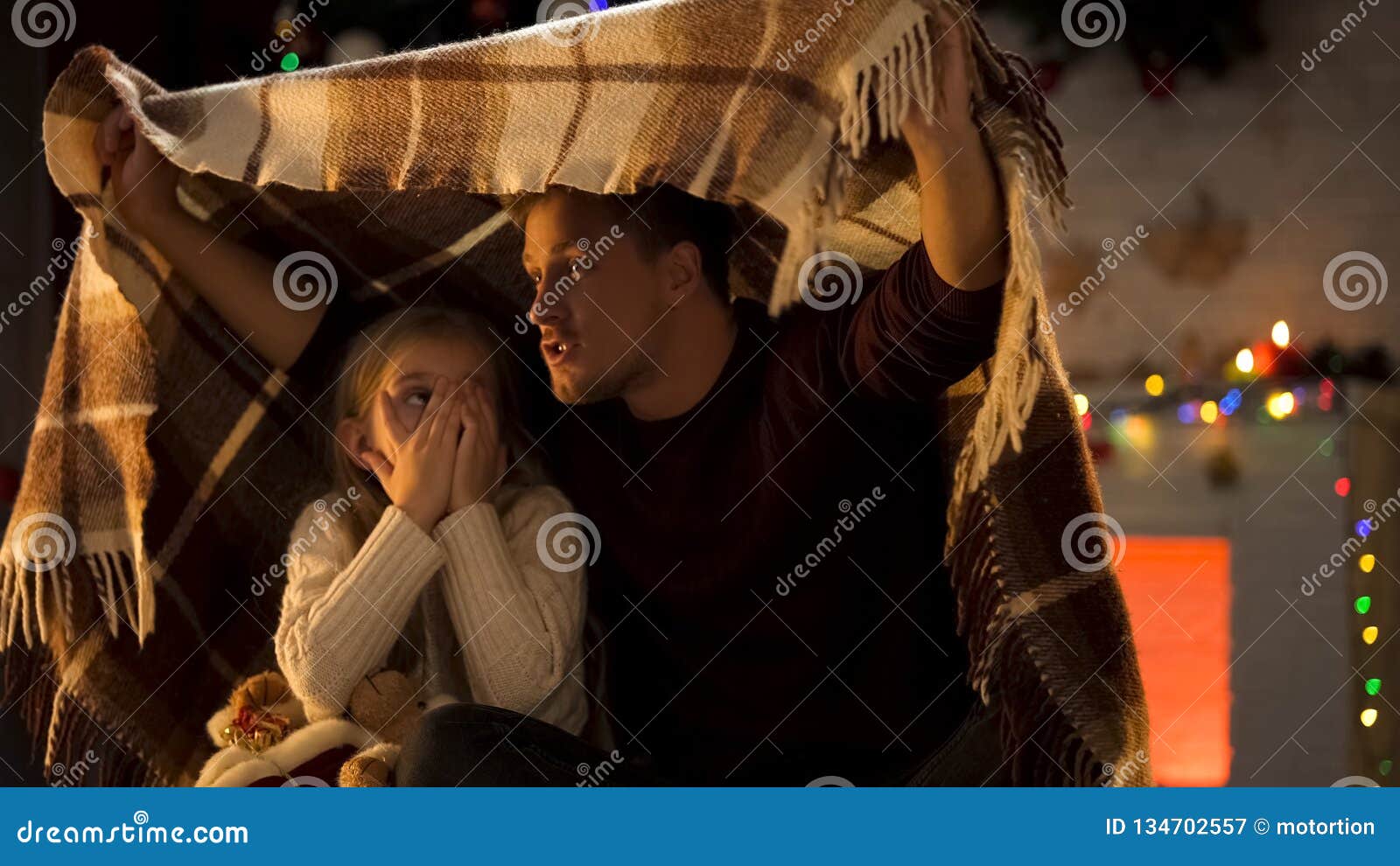 father telling horror christmas story for little girl sitting under cozy plaid