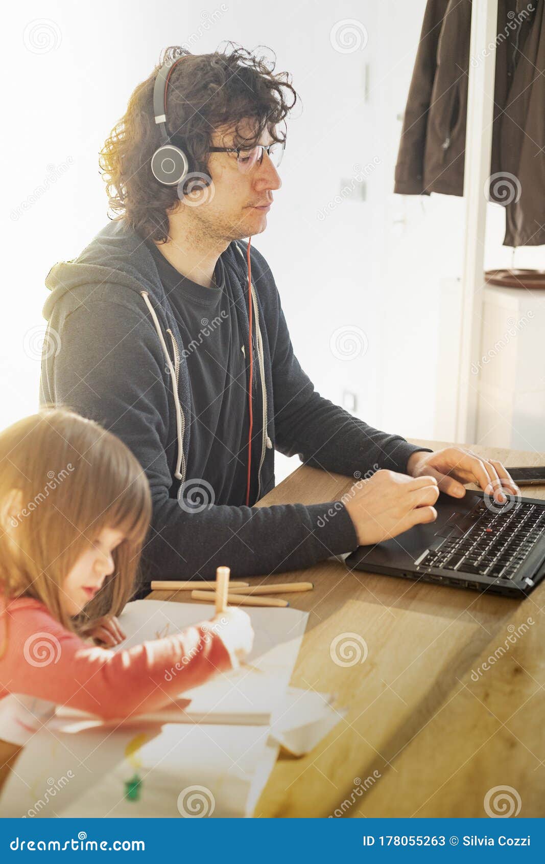 father working from home with little daughter during covid-19 lockdown. vertical shot with flare