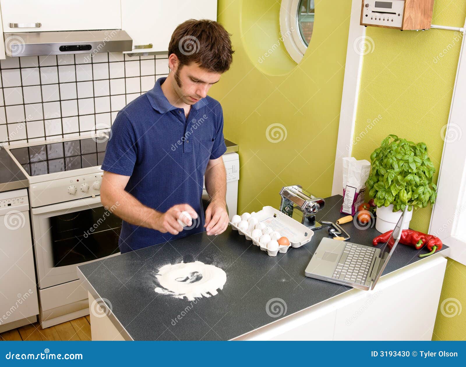 Fazendo a massa - receita em linha. Um homem novo que faz a massa em casa em uma cozinha do apartamento usando uma receita do computador