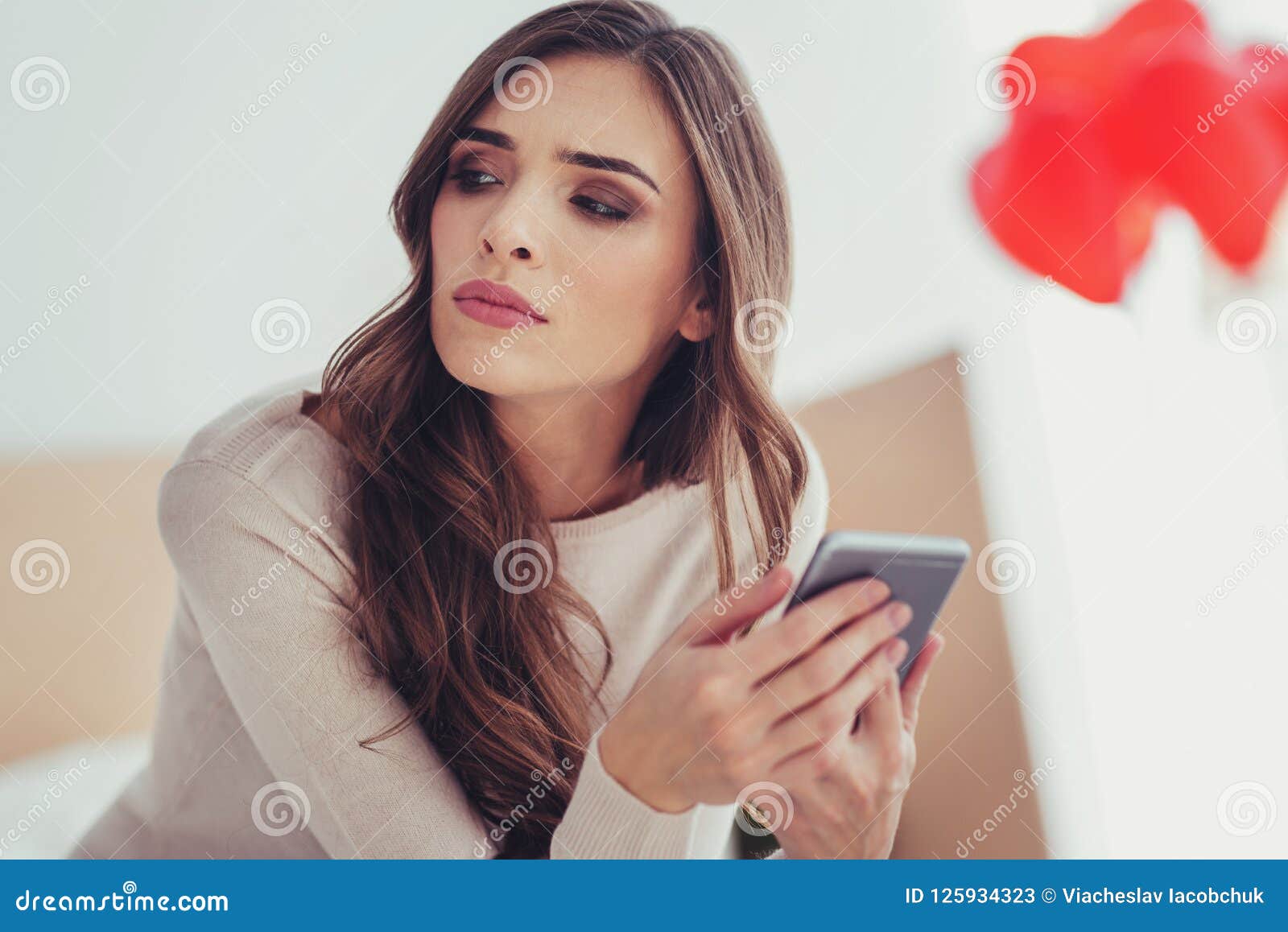 Feche acima da moça que olha afastado com um telefone celular nas mãos. Perdido nos pensamentos Feche acima da menina atrativa nova que olha ausente ao guardar o telefone celular nas mãos e ao esperar a data com seu noivo