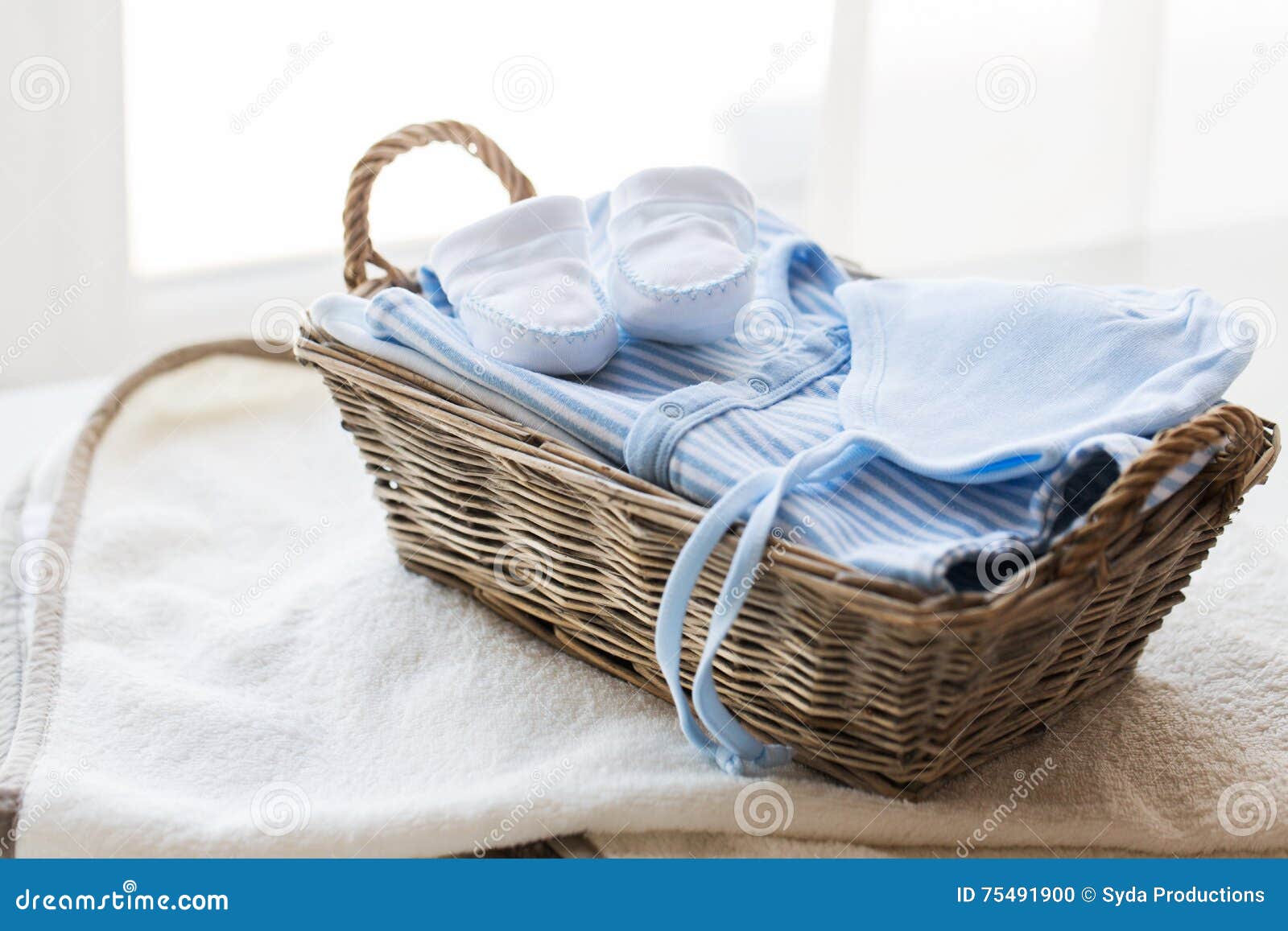 Feche acima da roupa do bebê para o menino recém-nascido na cesta. Roupa, primeira infância, maternidade e conceito do objeto - próximo acima dos sapatinhos de lã brancos do bebê com a pilha da roupa e da toalha para o menino recém-nascido na cesta na tabela
