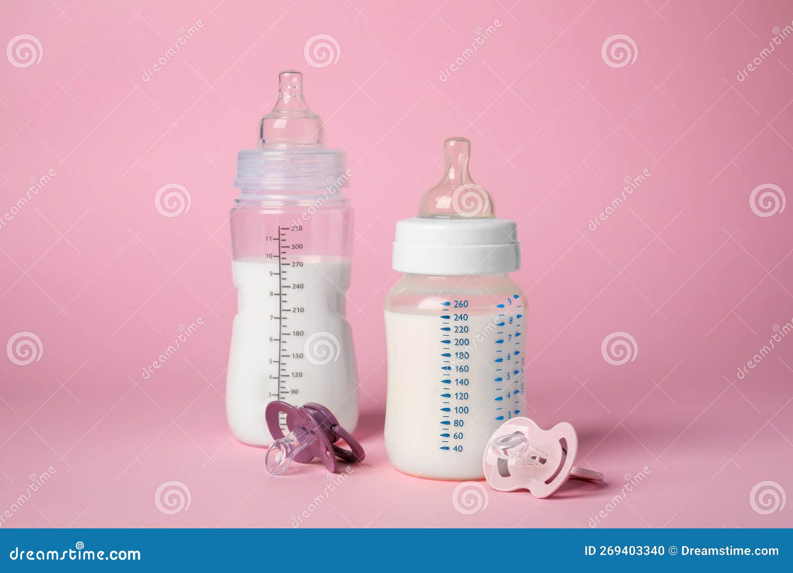 Feeding Bottles with Milk and Baby Pacifiers on Pink Background Stock