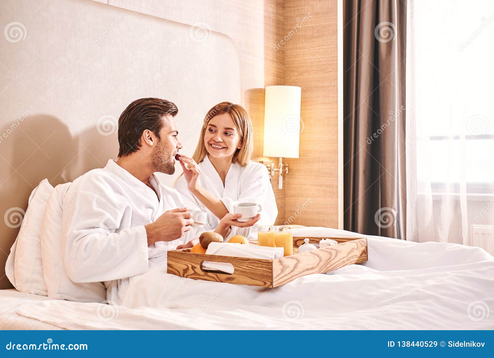 Feeding Each Other Couple Are Eating In Hotel Room Bed Stock Image