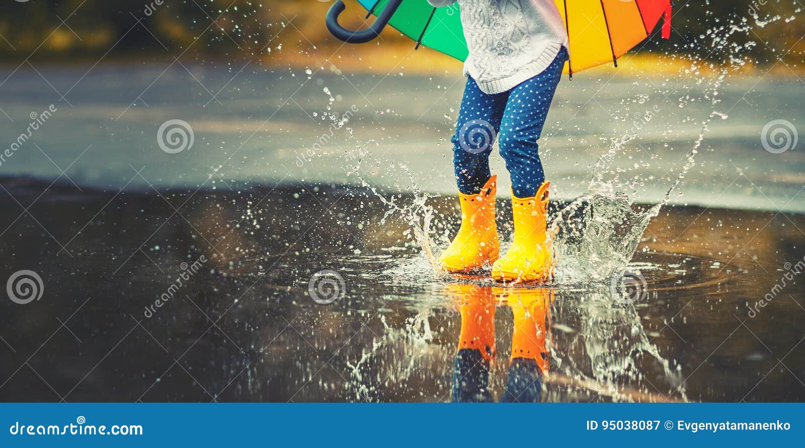 feet of child in yellow rubber boots jumping over puddle in ra